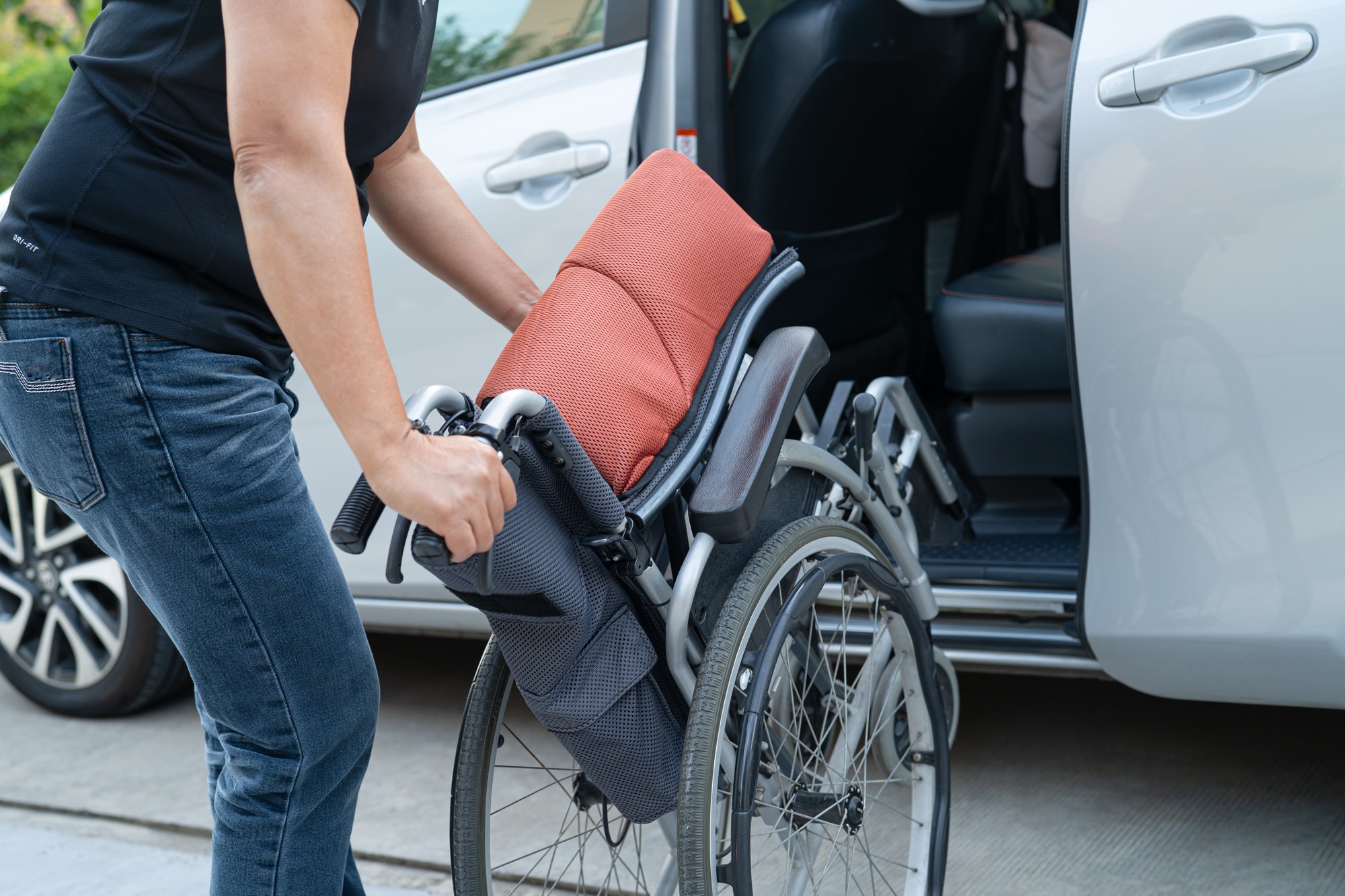 Asian woman folding and lift up wheelchair into her car. Accessibility concept.