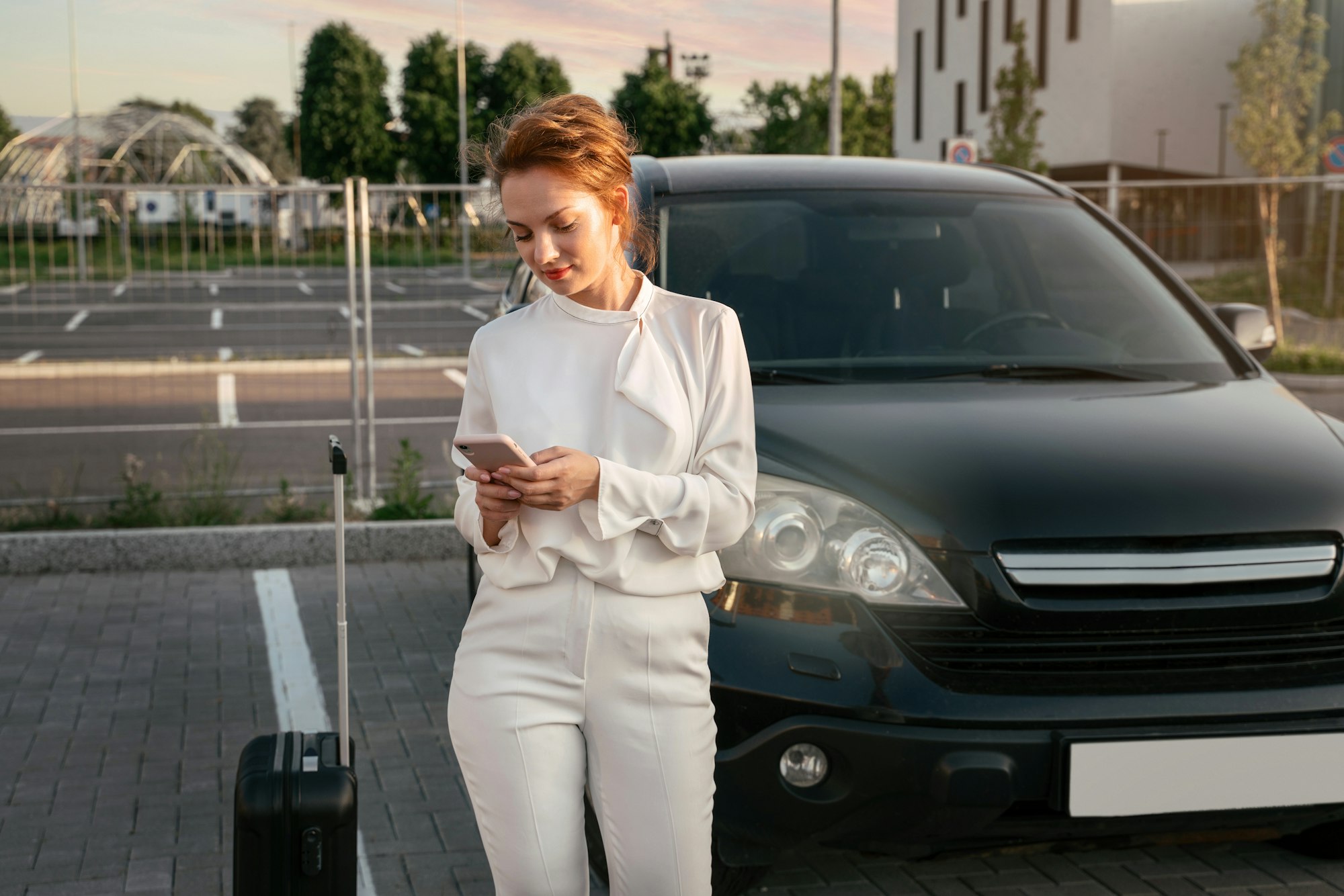 Businesswoman with travel bag using mobile phone, booking tickets standing near car